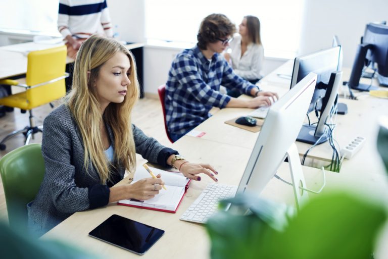 employees working on their macs while their colleagues talk in the background