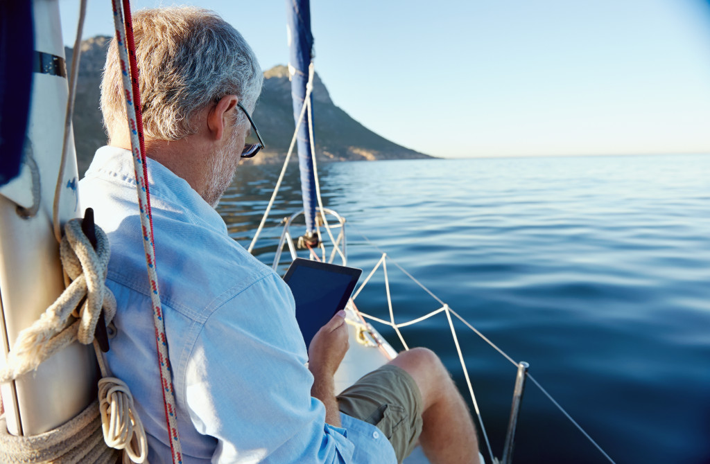 sailing man reading tablet computer on boat with modern technology and carefree retired senior successful lifestyle