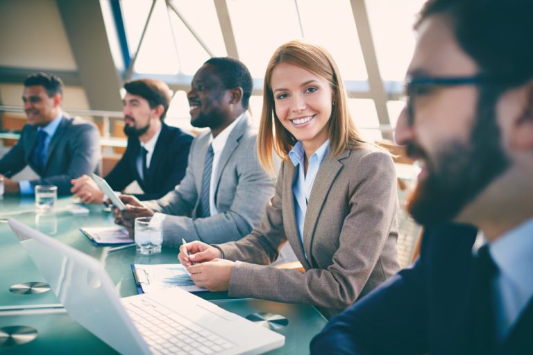 business people listening to presentation at seminar with focus on smiling woman looking at camera