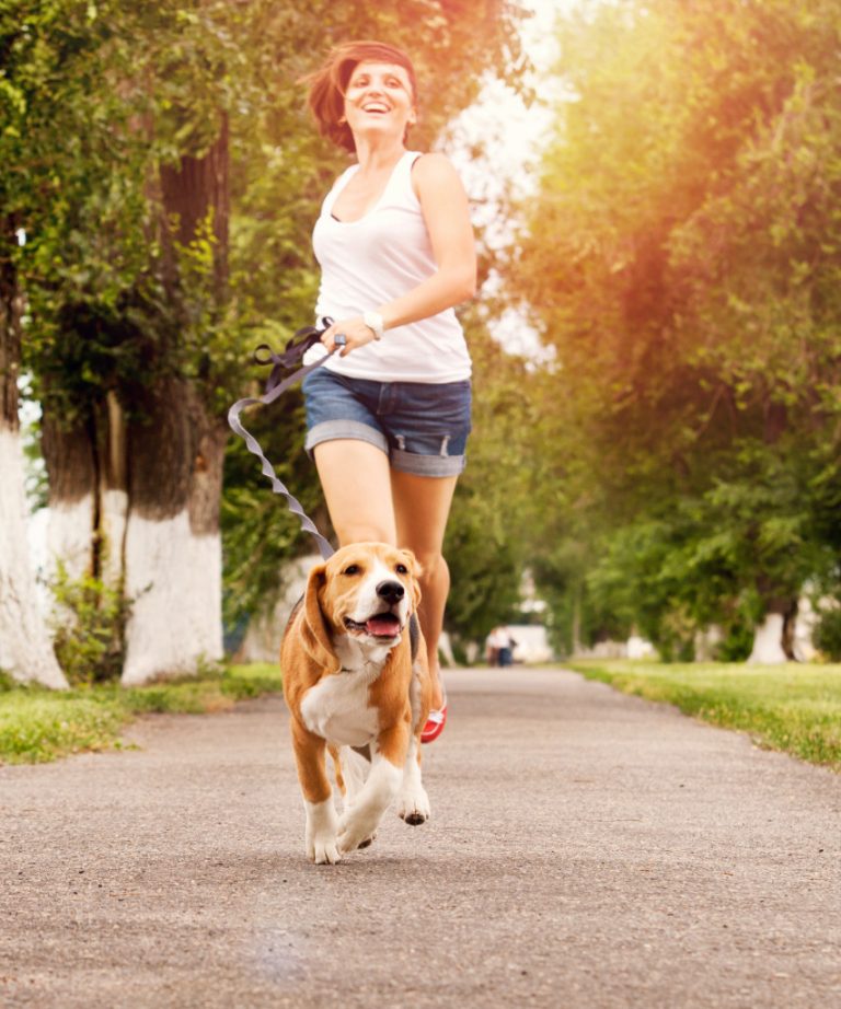 A woman happily runs with her beagle out on the street