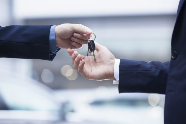 salesman handing car keys to businessman car purchase at store